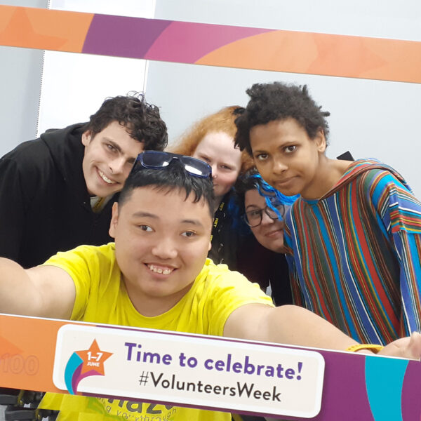 A small group of Amazing Futures volunteers posing with a cardboard cut-out frame to celebrate Volunteers Week.