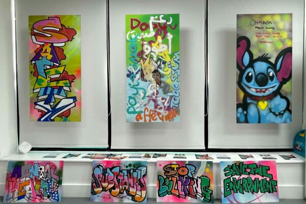 Three brightly coloured graffiti style artworks on display in a gallery, including one featuring Stitch from the Disney film Lilo and Stitch.