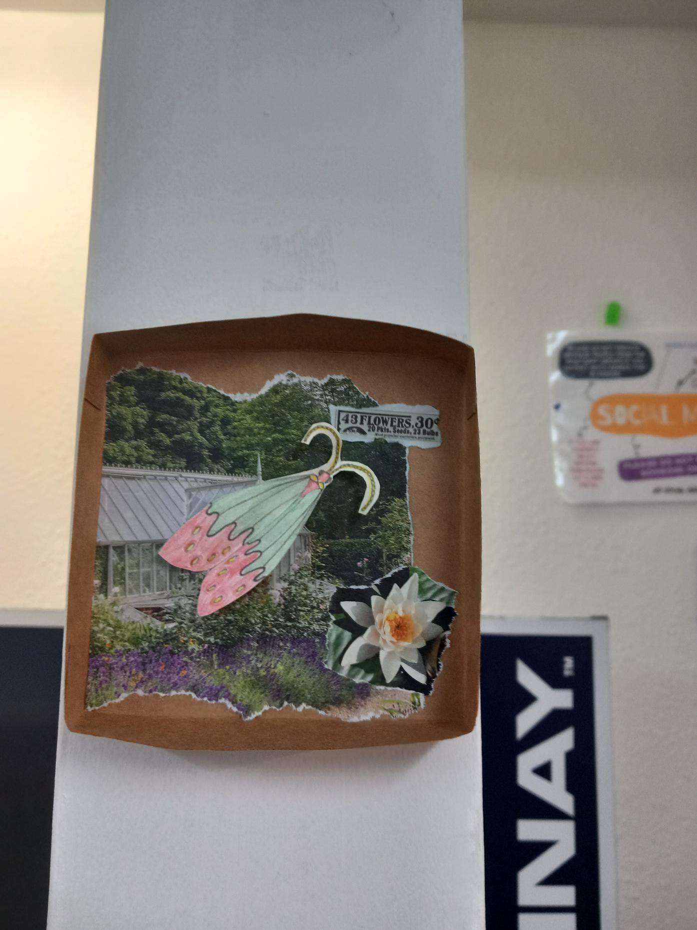 Media (14) Bug box with a page from a magazine with a large photo of a small building surrounded by greenery, with a photo of a lily cut out of a magazine, and a paper bug with blue and red wings and curly antennae.