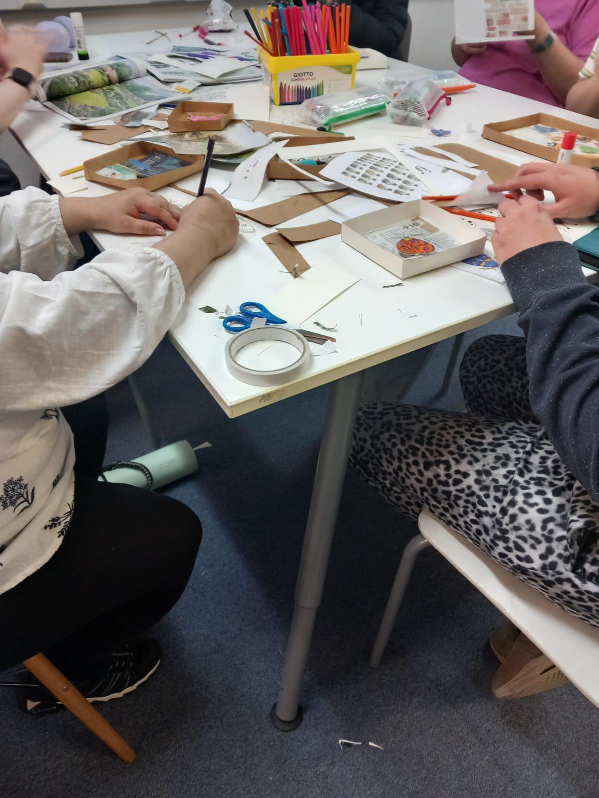 Media (18) Young people sat at a table making their bug boxes. There are magazines and printed out pictures on the table, cut into pieces.