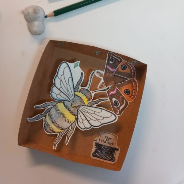 A shallow box with a large paper bee, and a smaller butterfly and typewriter