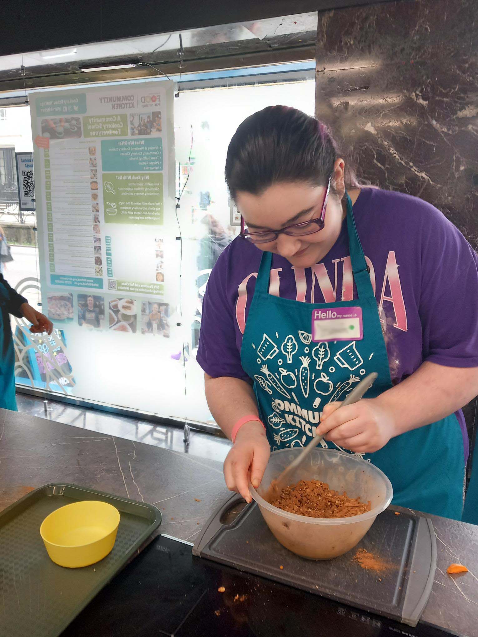shared image (2) blur A young person in a purple Glinda t-shirt mixing the energy ball ingredients in a bowl at our baking session.