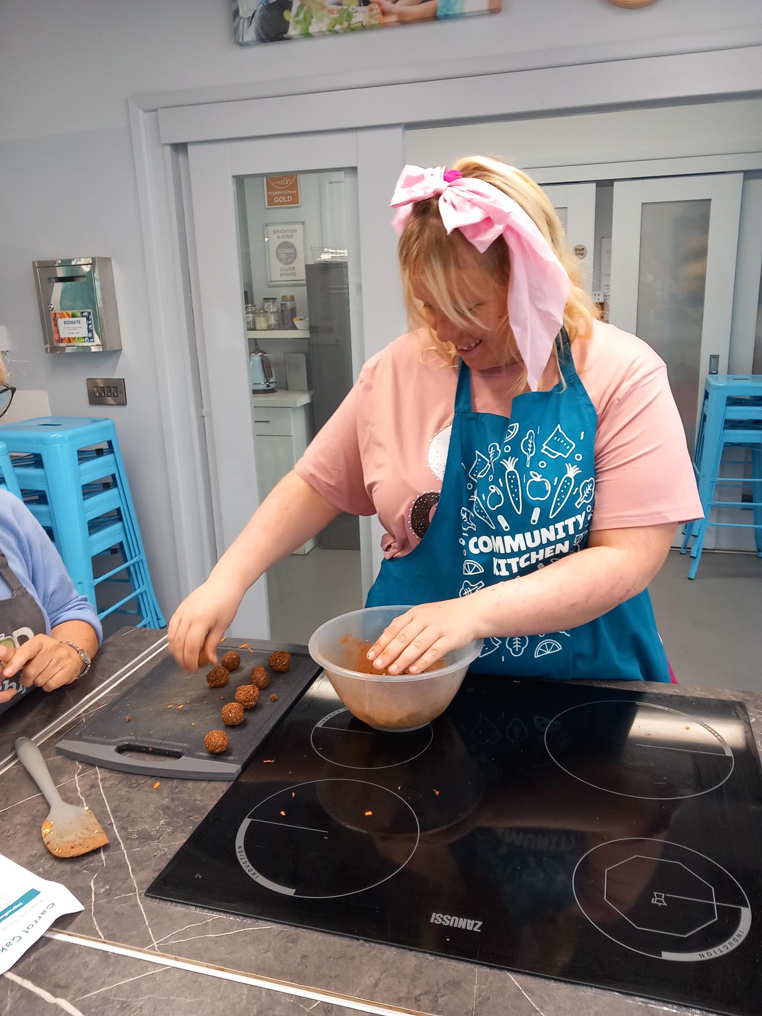 shared image A young person with a light pink bow in their hair forming the energy dough ingredients into balls and placing them on a tray, at our baking session.