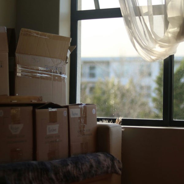 Moving boxes piled up in front of a window in a high rise flat.