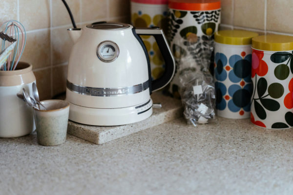 White kettle surrounded by colourful tea and coffee containers.