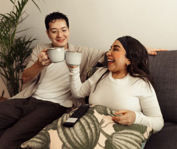 Woman and her friend or carer clink cups together, sitting on a sofa.