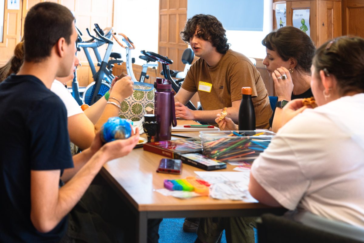 Group of young people sat around a table full of papers and colour pensils, eating pizza.