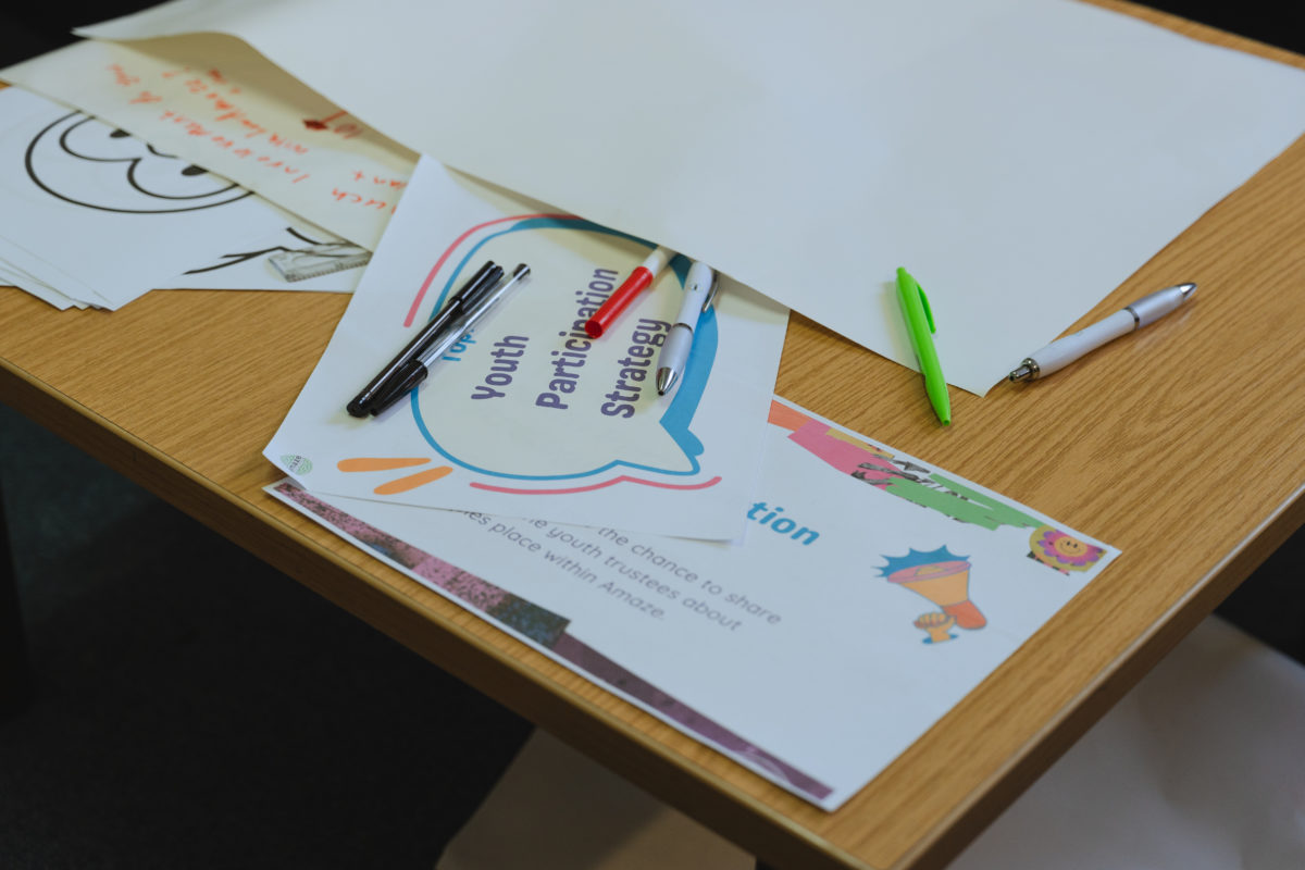Papers and pens on a table. One of the papers has a large speech bubble with text reading "Youth Participation Strategy".