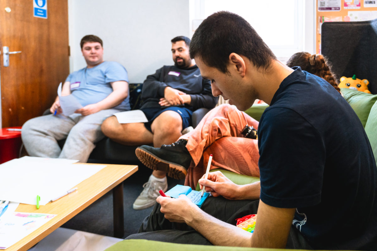 Small group of young people sat around a table, one is writing on a stack of post-it notes.