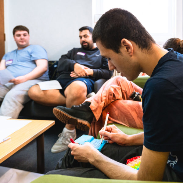 Small group of young people sat around a table, one is writing on a stack of post-it notes.