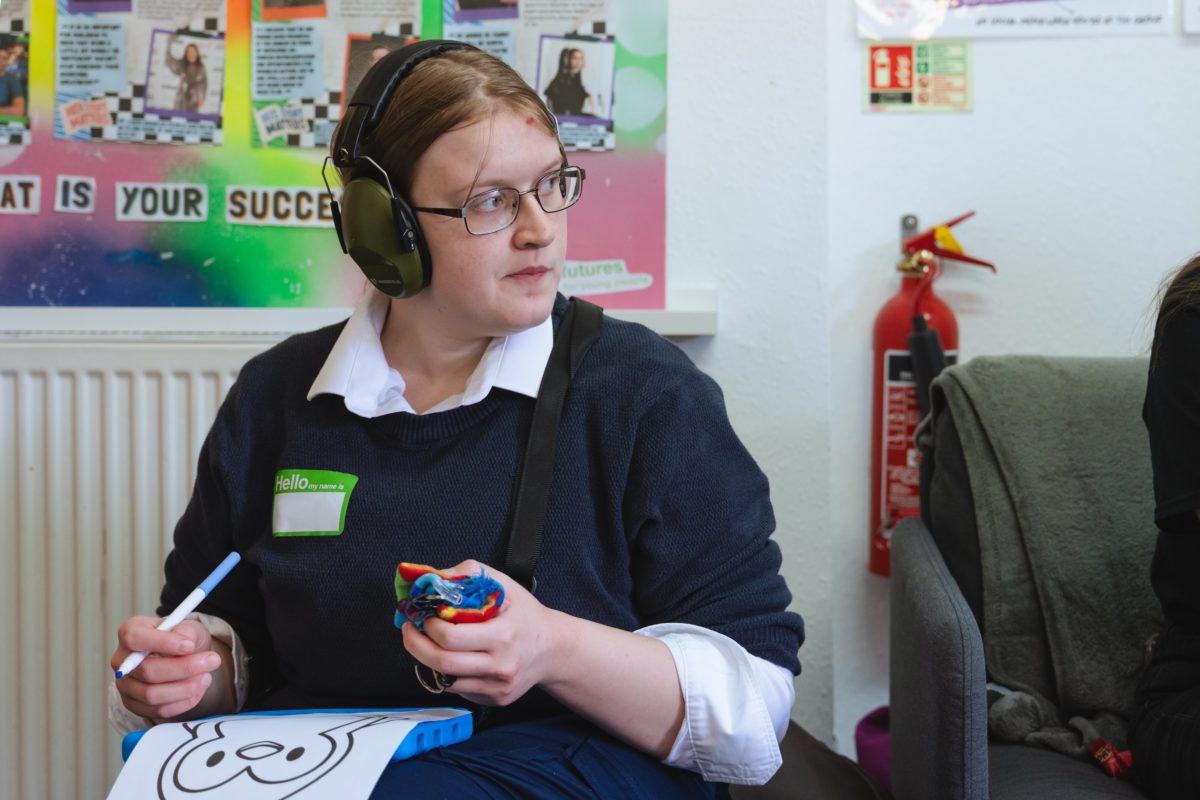 Young person in ear defenders holding a colouring pen and a print out of a penguin.