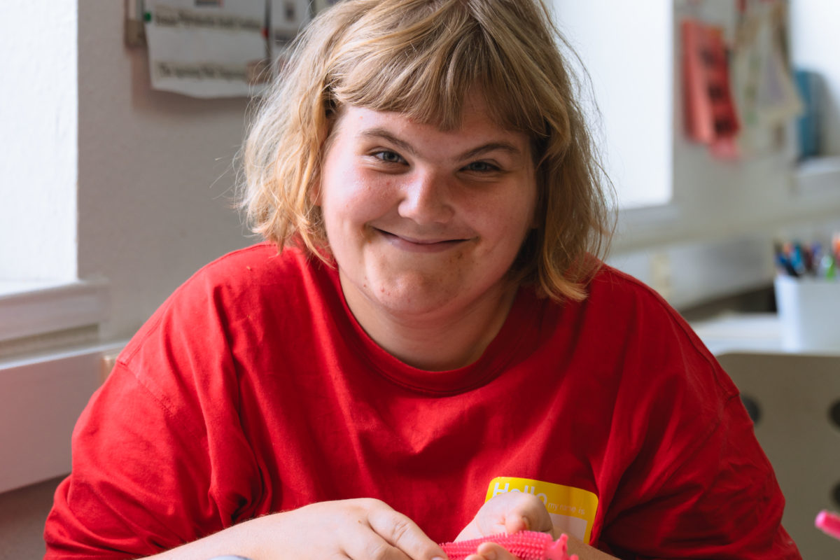 Young person smiling and holding a pink fidget toy.