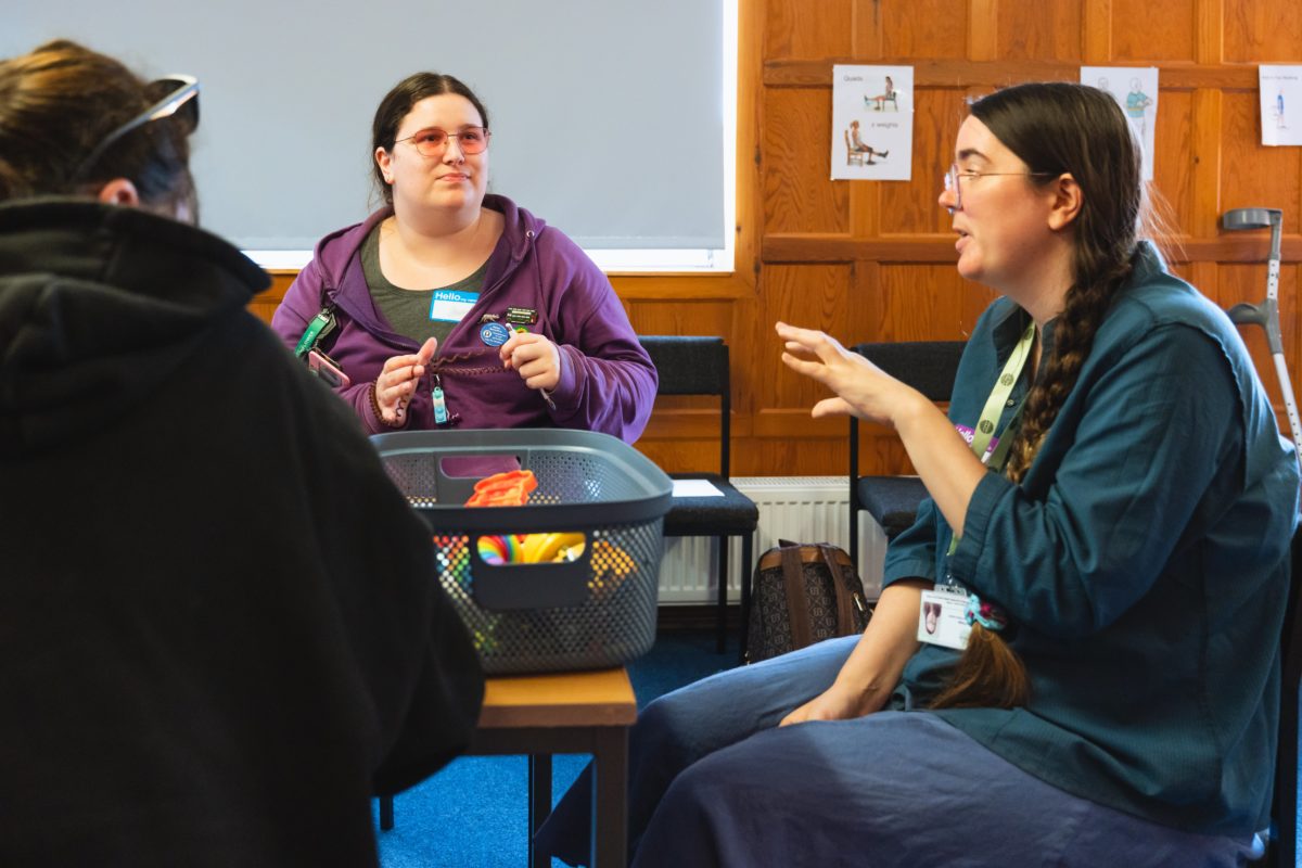 Rose from the Comms Team and a young person having a conversation. There is a tub full of fidget toys on the table between them.