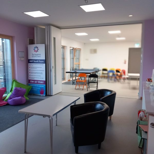 The main space. There are comfy padded chairs and folding chairs. It is a wide open space with lots of room. THere is a ping pong table, and brightly coloured beanbags.