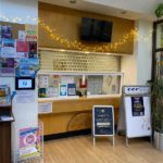 Reception area with a message board with lots of signs. There are string lights, and two stands with notices.