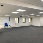 A large, empty room. There is one stack of chairs. Most of the light comes from lit ceiling panels.