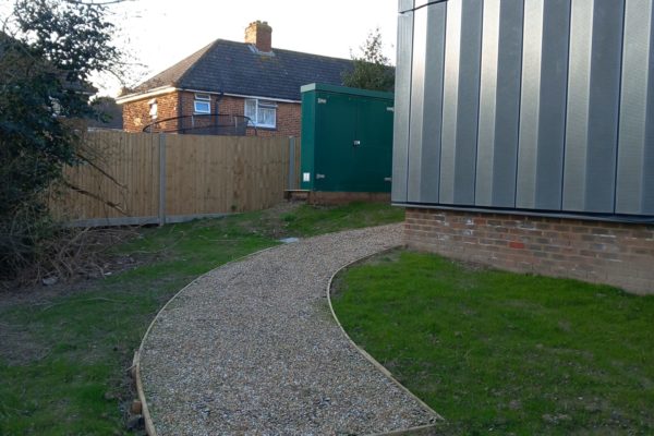 Close up on the start of the gravel path leading to the side door. It curves around the corner of the building.