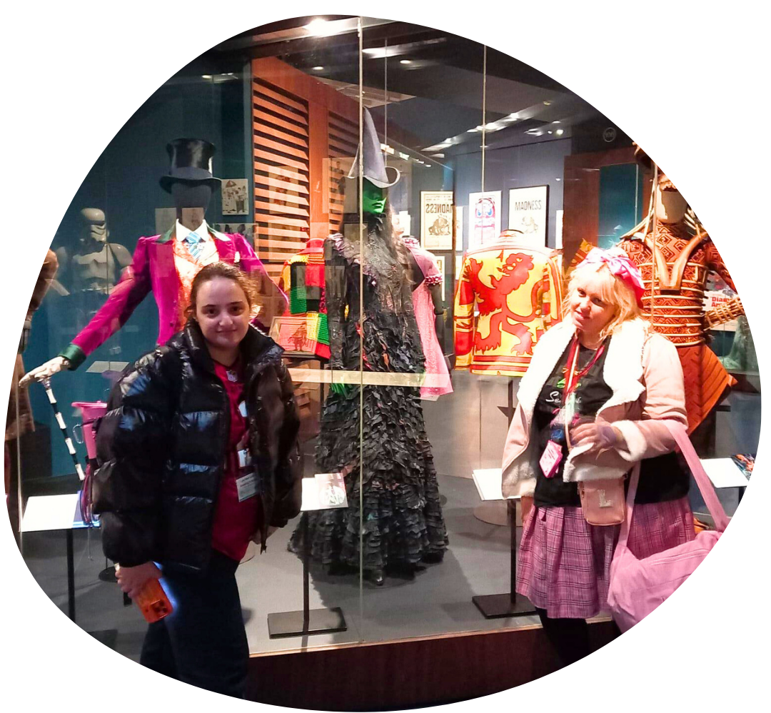 Two young people stood next to a costume display in the V&A Museum, featuring Elphaba's costume from Wicked.