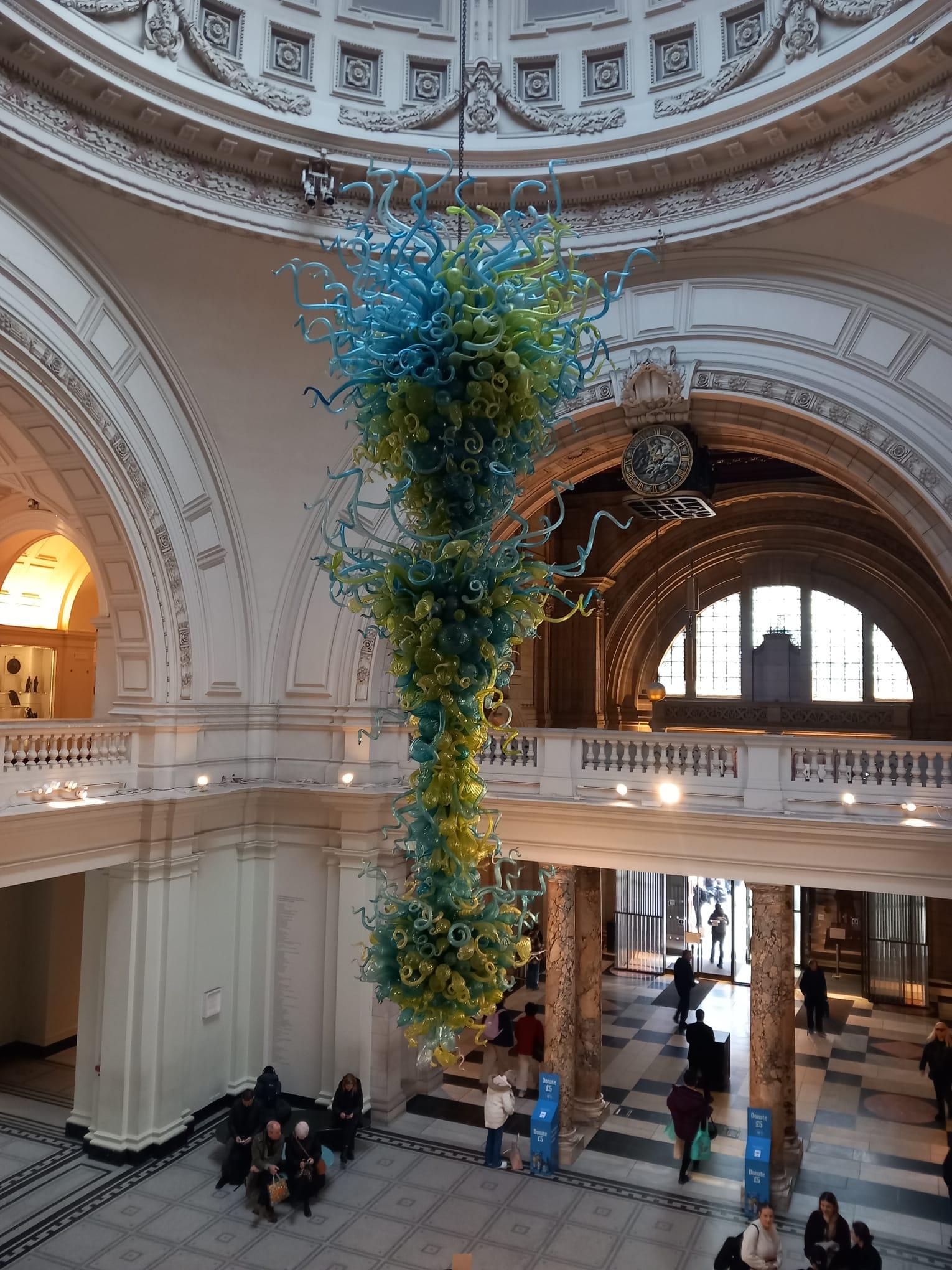Hanging chandelier-style artwork, made of green and blue bubbles and tentacle-like fronds. It hangs in the middle of the museum foyer.