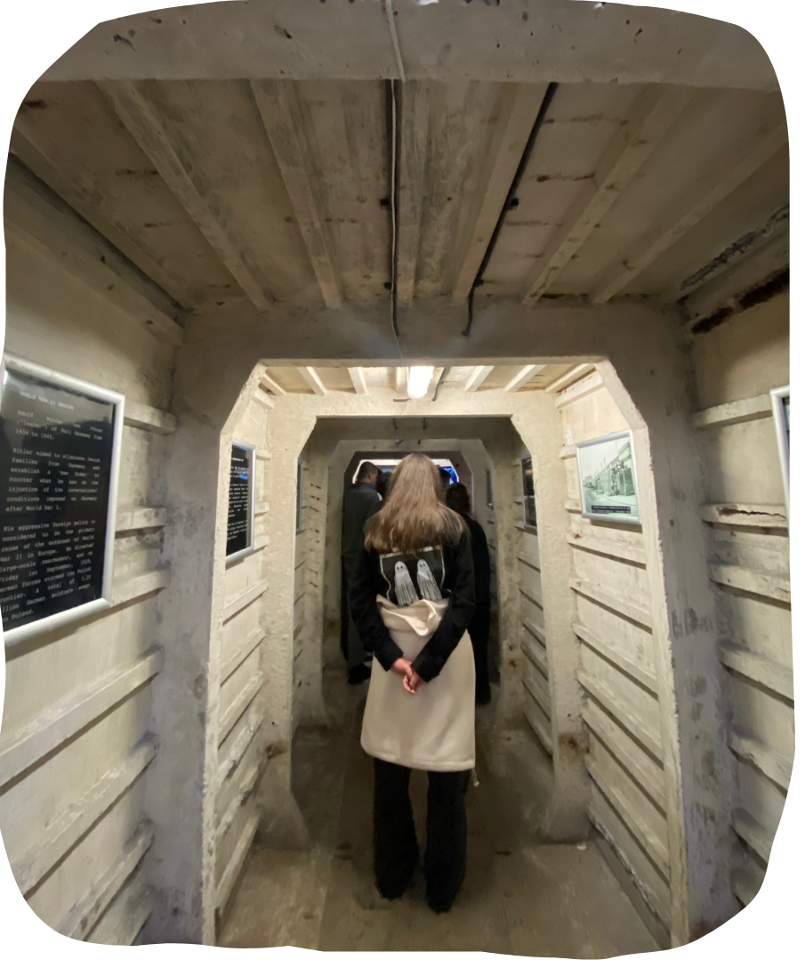 Young person walking through a tunnel, with solid concrete struts, and framed displays on the walls.