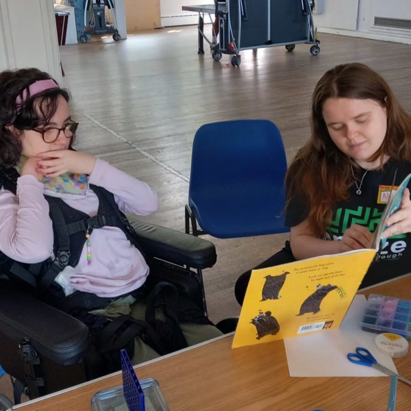 Amaze youth worker reading to a young person using a power chair.