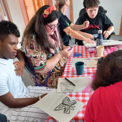 3 Young people sat at a table designing their shapes to cut out for the cyanotype workshop.