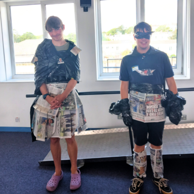 9 Young people wearing clothes they designed for the fashion show. The clothes are made of newspaper and bin bags, and are worn over their regular clothes.