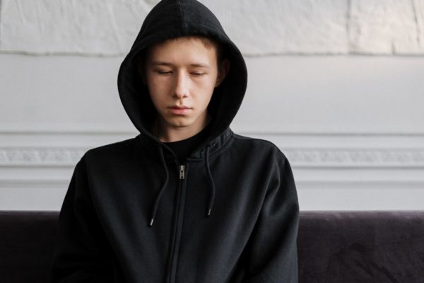 Unhappy teen boy in hoodie, sat alone on sofa.