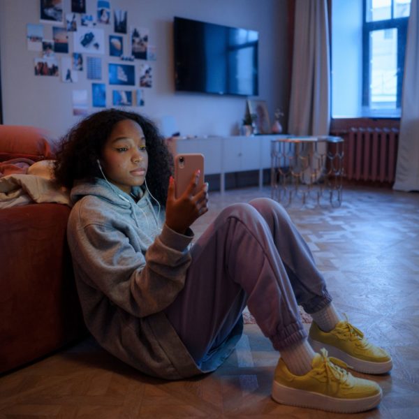 Teen girl sat alone in her bedroom, looking unhappily at her phone