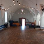 Inside St. Cuthman's Church hall. It's a big, open space, with different seating options. There are lights strung between the eaves.