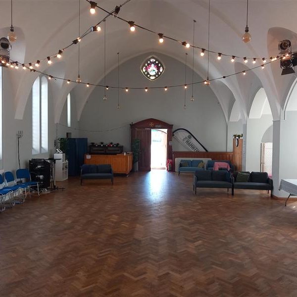 Inside St. Cuthman's Church hall. It's a big, open space, with different seating options. There are lights strung between the eaves.