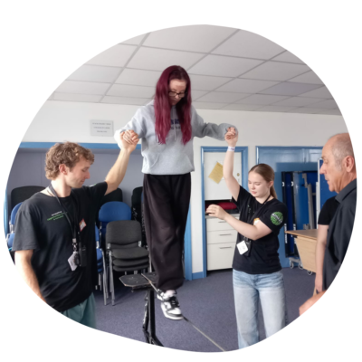 A young person walking on a tightrope several feet above the ground, with two youth workers holding their hands to help them balance.