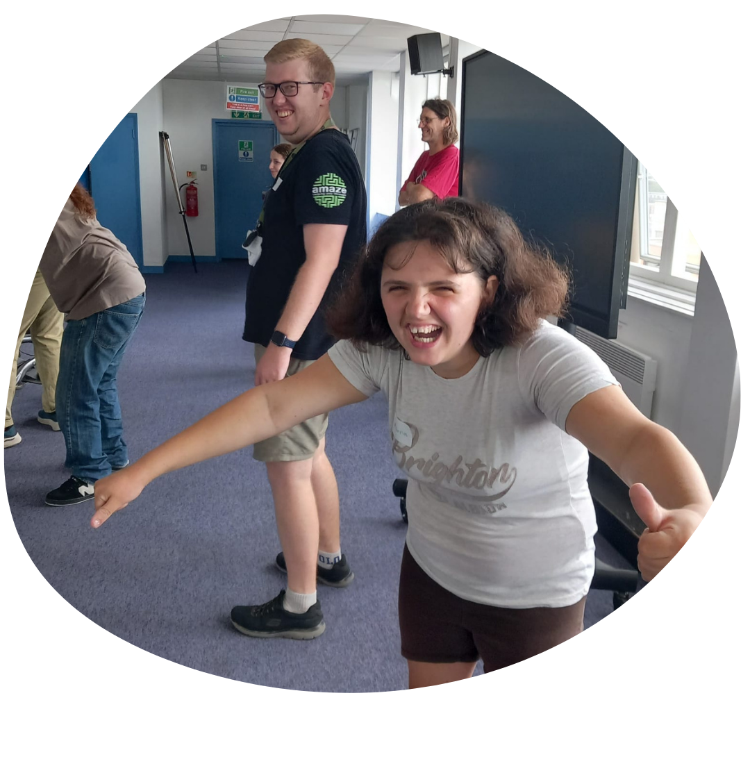 A young person with their arms out, laughing, in the middle of a game, while a youth worker in an Amaze tee looks on, smiling.