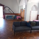 Inside the venue - a large open space with a wooden floor, tall ceilings and a lot of light. There are several padded two-person seats with cushions.
